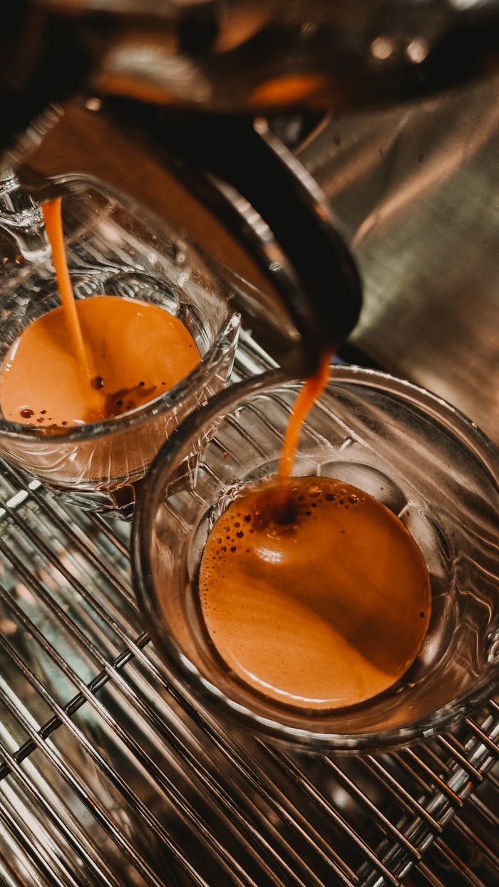 services-02 Rich espresso flowing into glass cups on a metallic espresso machine tray.