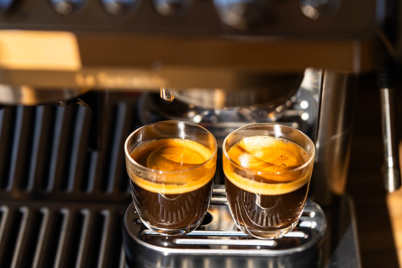 hero-img Two freshly brewed espresso shots under a modern coffee machine, highlighting crema and rich aroma.