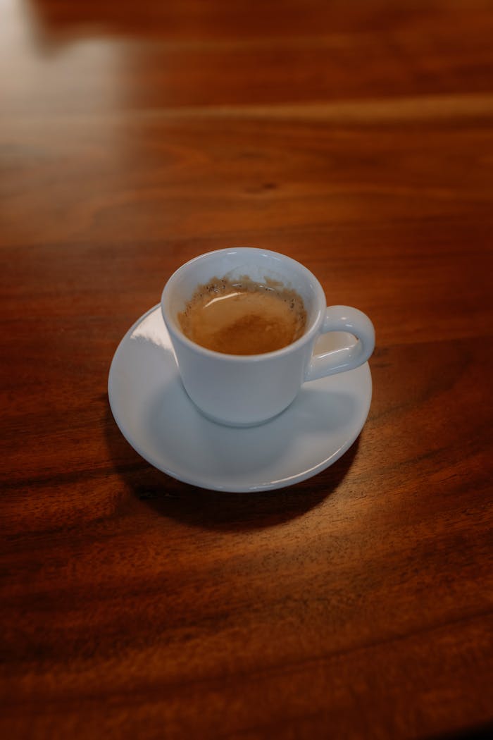 about-01 Warm espresso served in a white cup on a rich brown wooden table, inviting and aromatic.